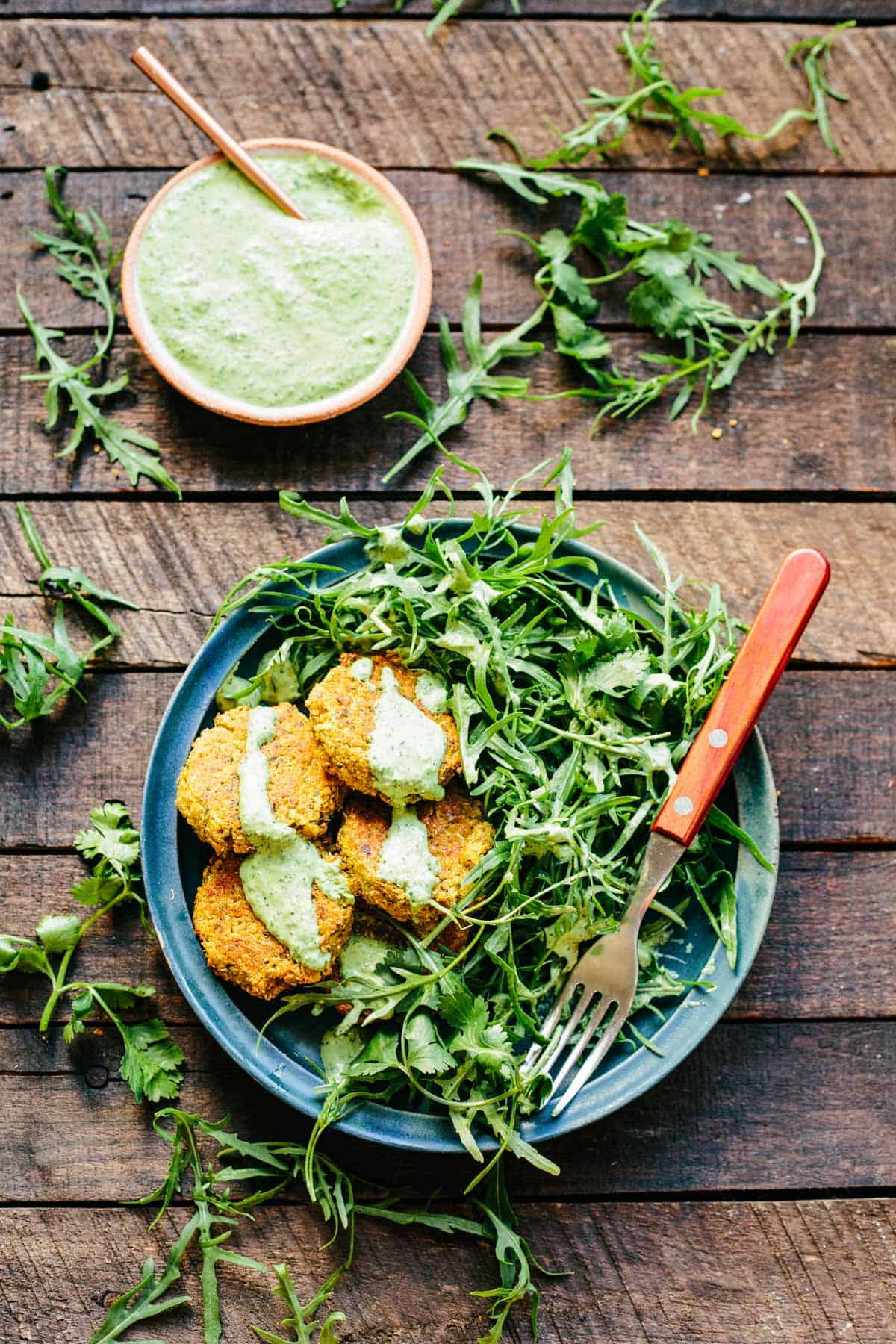 Plate loaded with salad greens and quinoa falafel drizzled with green tahini.
