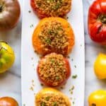 Overhead shot of a long white plate with four red and yellow tomatoes with breadcrumbs on top.