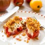 Close up of a baked goat cheese stuffed tomato cut in half on a plate with a knife and fork.