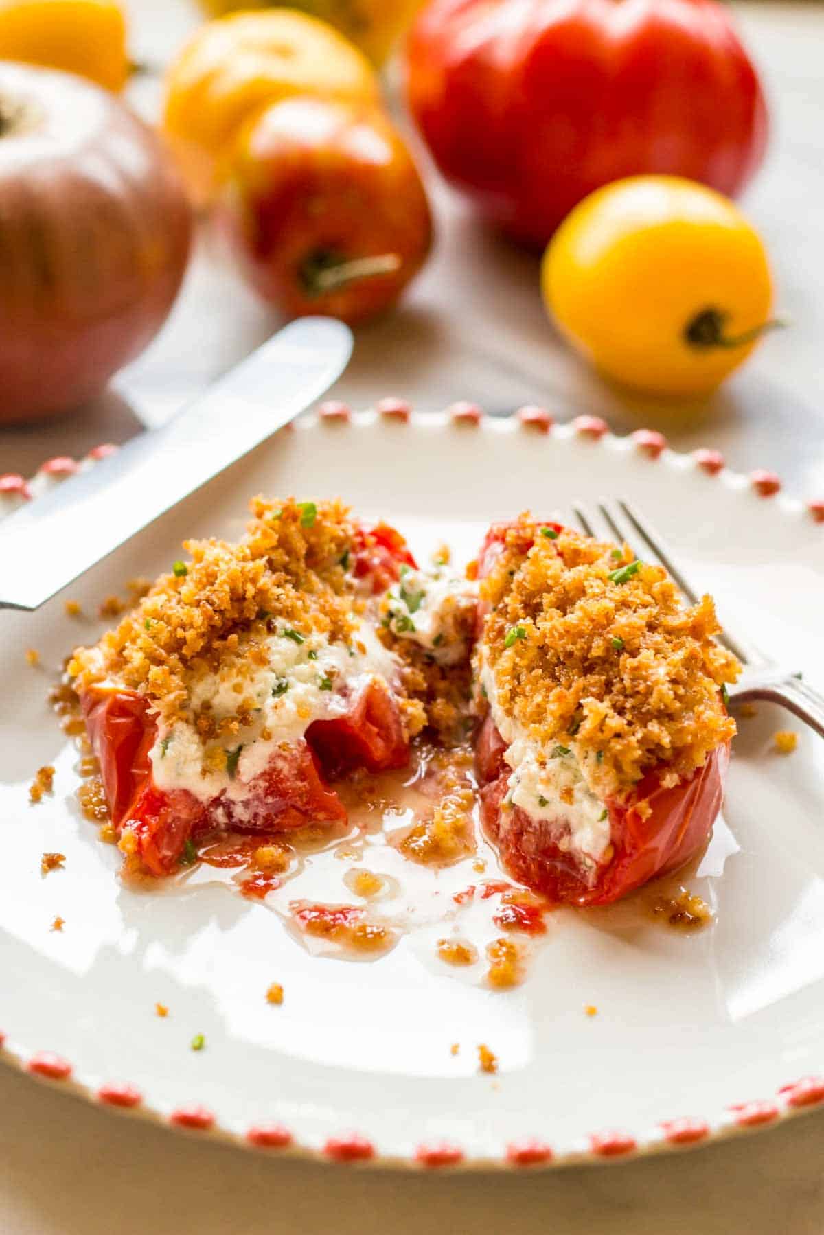 Close up of a baked goat cheese stuffed tomato cut in half on a plate with a knife and fork.