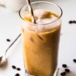 A tall glass of iced coffee with a straw and coffee beans in the background.