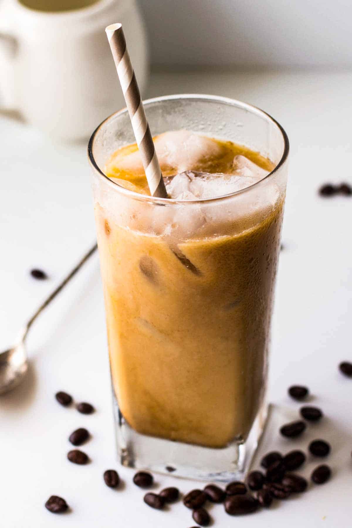 a tall glass of iced coffee with a straw and coffee beans in the background