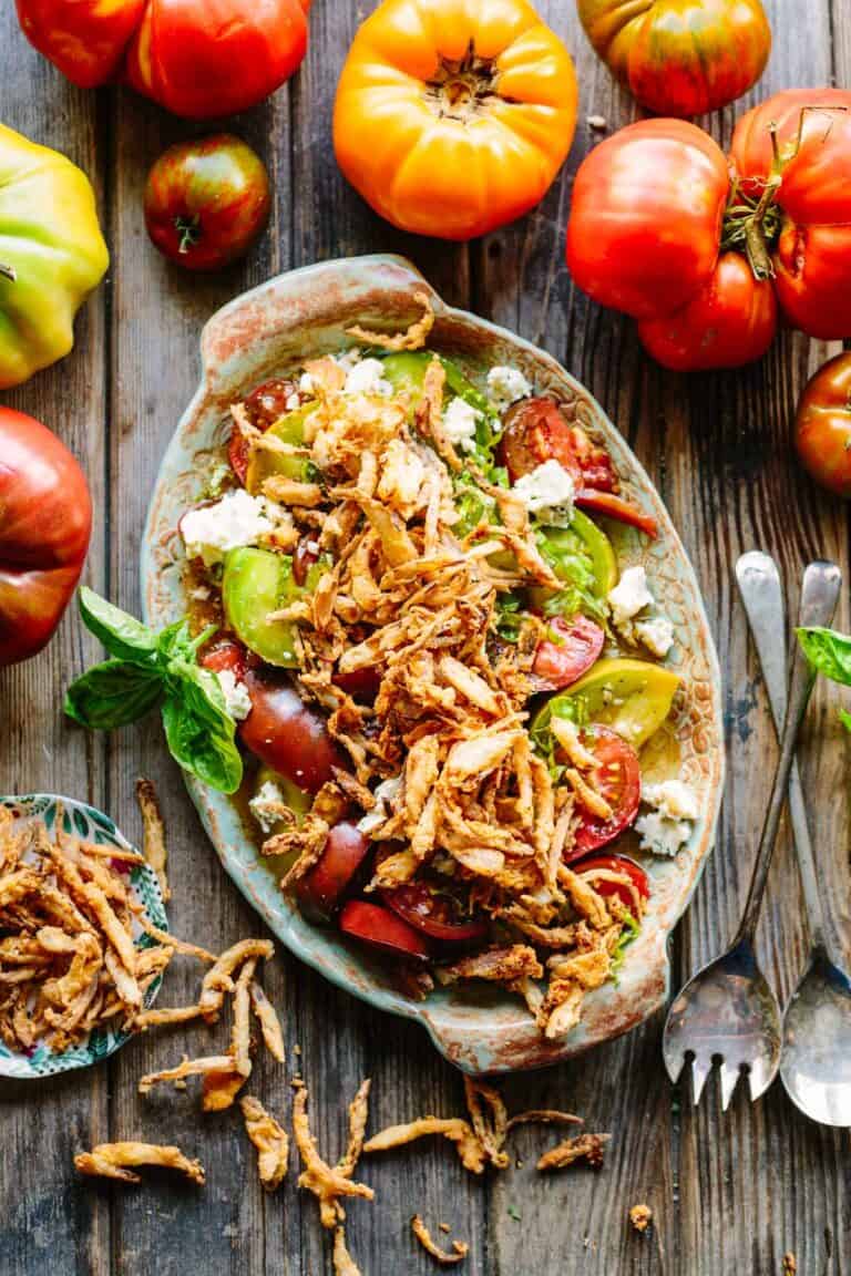 Overhead shot of a platter of tomatoes with fried onions on top.