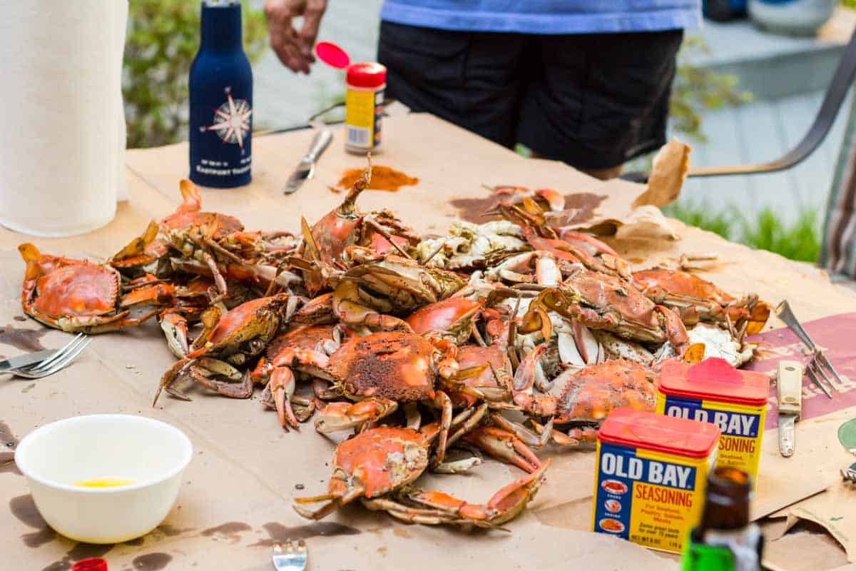 Freshly steamed crabs on brown paper with cans of Old Bay Seasoning.