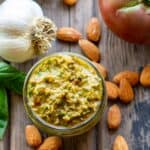 Overhead shot of a jar of pesto with whole almonds and garlic scattered around.