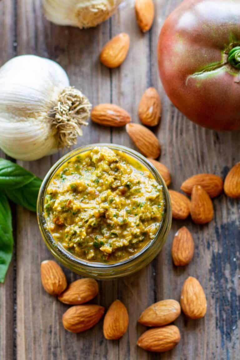 Overhead shot of a jar of pesto with whole almonds and garlic scattered around.