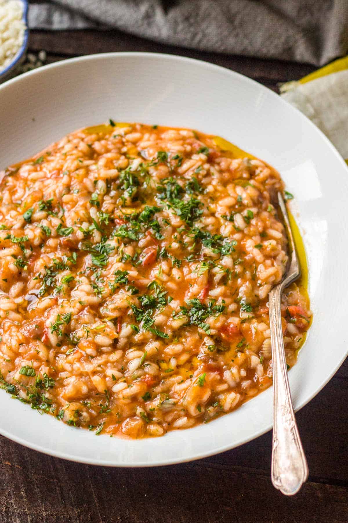 Close up of a shallow white bowl with tomato risotto and fresh herbs.