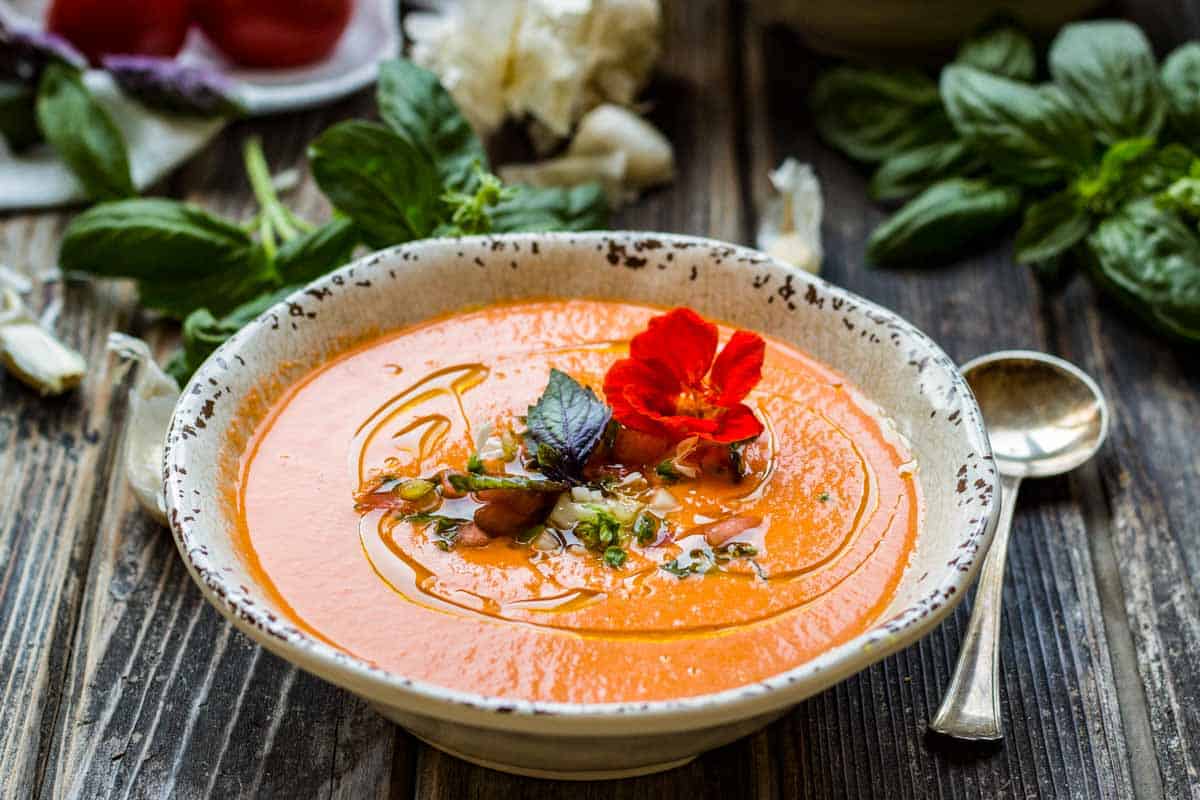 A bowl of watermelon gazpacho garnished with herbs and a flower.