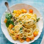 A bowl of spaghetti with sun gold tomatoes and basil on a blue background.