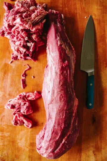 A whole beef loin on a wood cutting board with a knee and trimmings.