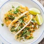 Overhead shot of 3 tacos garnished with cilantro and lime wedges on the side.