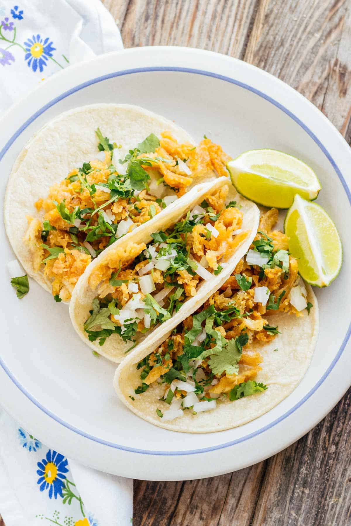 Overhead shot of 3 tacos garnished with cilantro and lime wedges on the side.