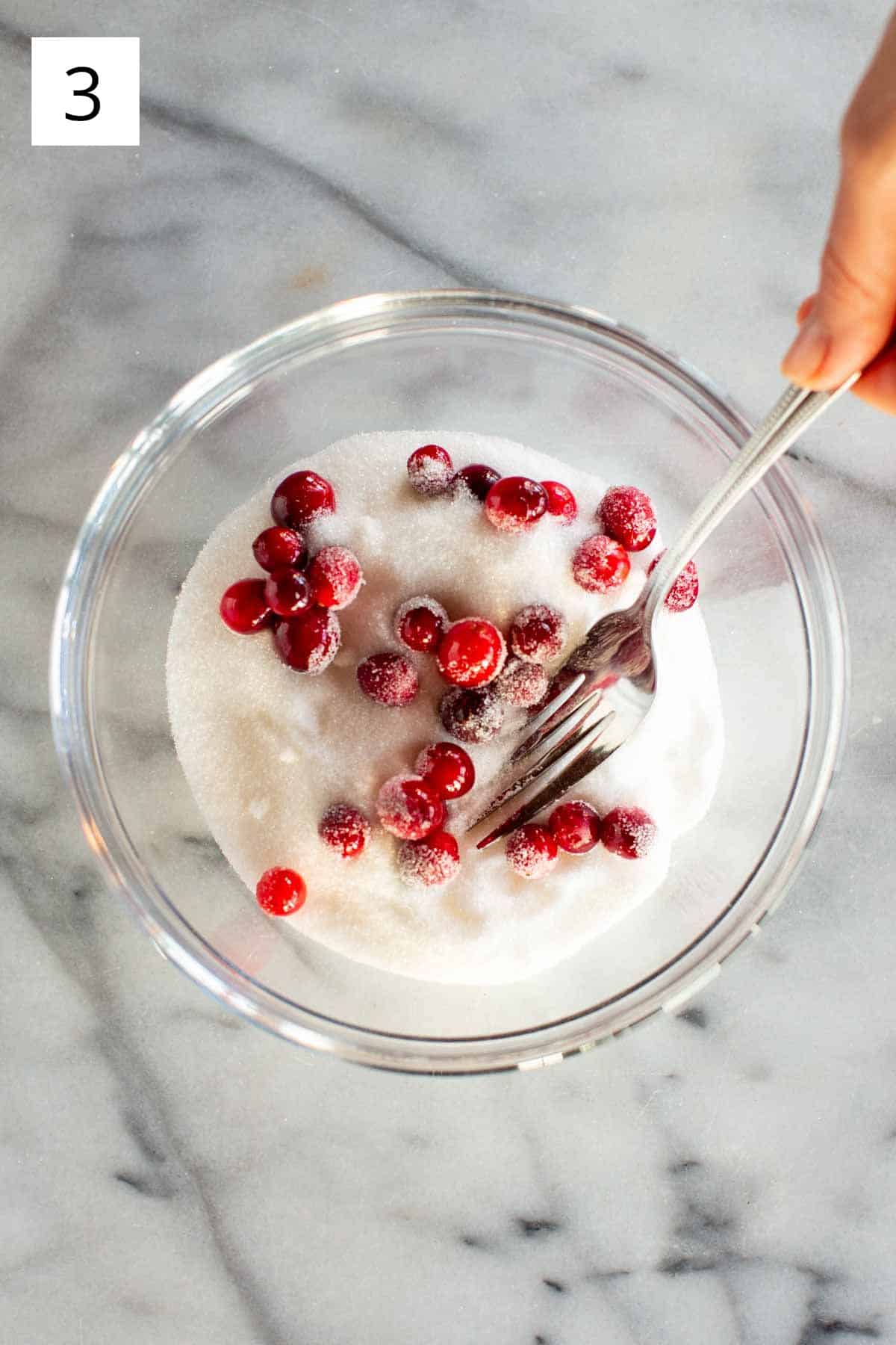 A bowl of sugar with cranberries and a fork.