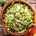 Overhead shot of a big kale apple salad in a wooden bowl with gold cutlery.