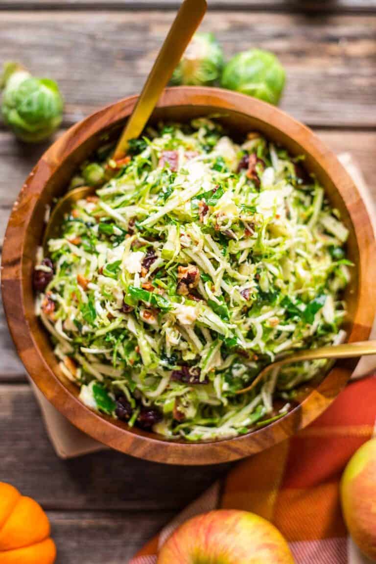 Overhead shot of a big kale apple salad in a wooden bowl with gold cutlery.
