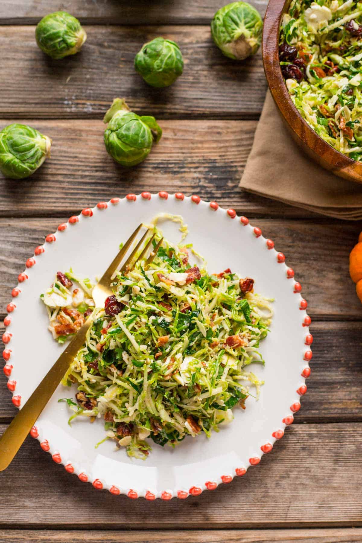 Overhead shot of a white plate on a wooden board with salad, a gold fork, and whole Brussels sprouts in the background.