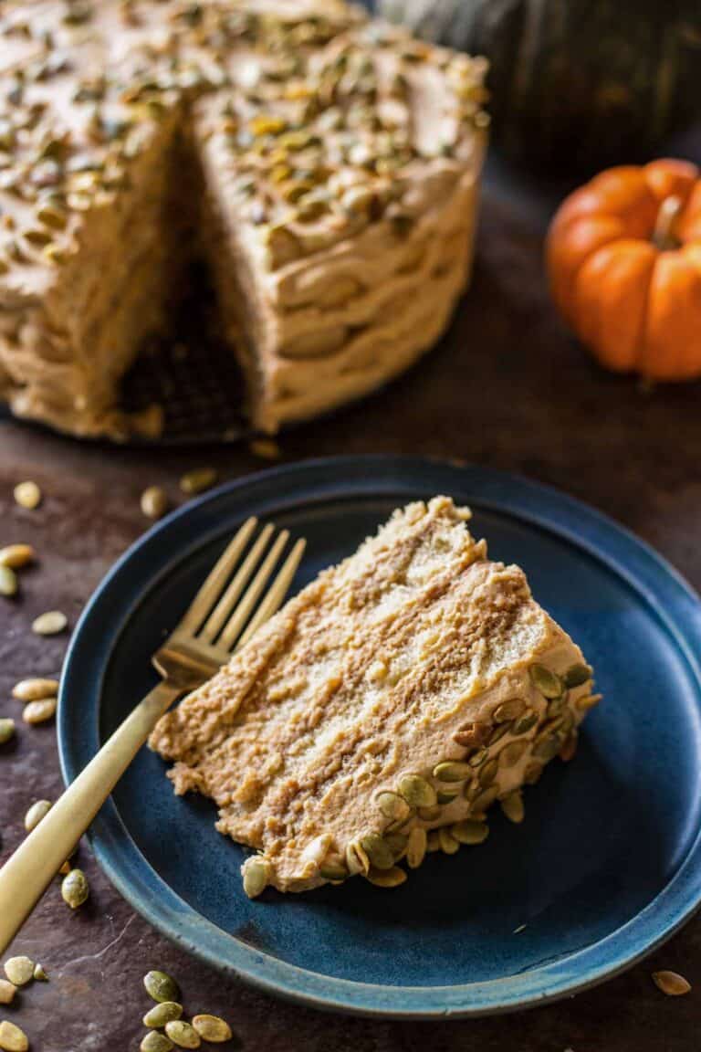 A slice of pumpkin tiramisu on a blue plate with the cake and pumpkins in the background.