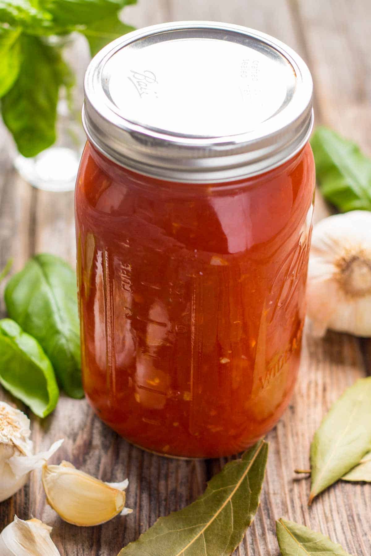 A mason jar of marinara sauce with garlic and basil in the background.