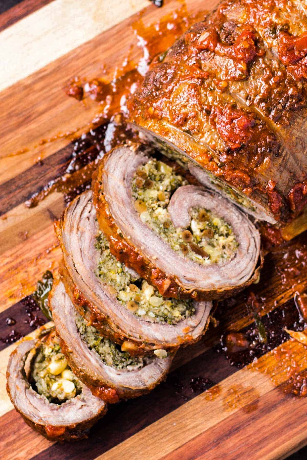 Overhead shot of a wooden cutting board with a large braciole being sliced into pinwheels.