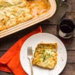 Top view of a corner slice of lasagna bolognese on a white dinner plate with a fork.