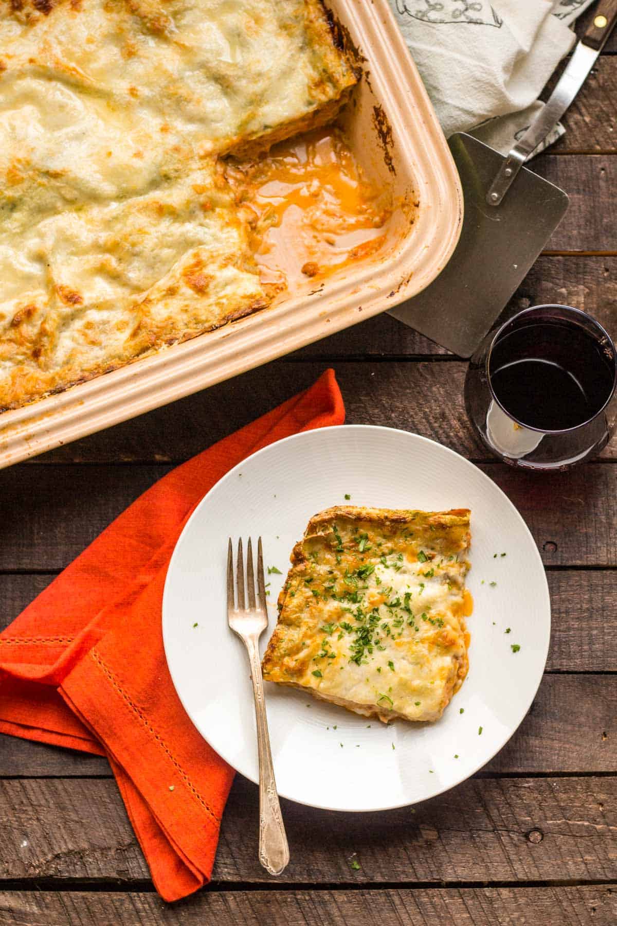 Top view of a corner slice of lasagna bolognese on a white dinner plate with a fork.