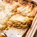 A spatula lifting a slice of lasagna bolognese from a stoneware baking dish.