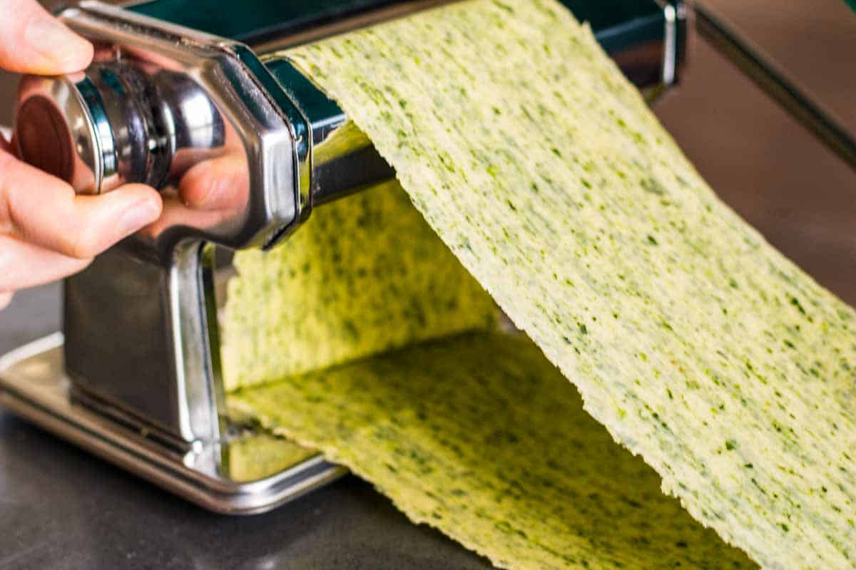 A fresh lasagna noodle being fed through a manual pasta machine.