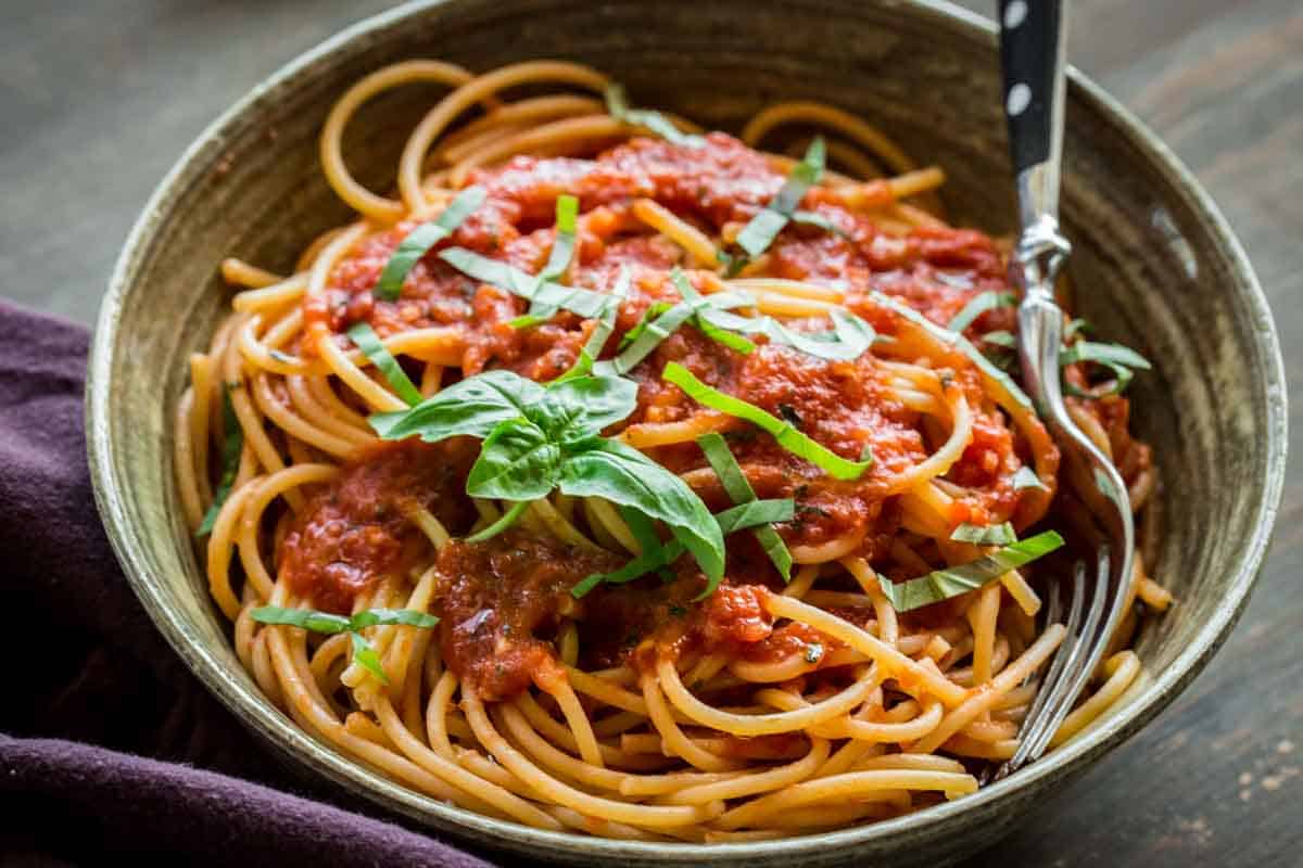 A bowl of spaghetti with marinara sauce and fresh basil on top.