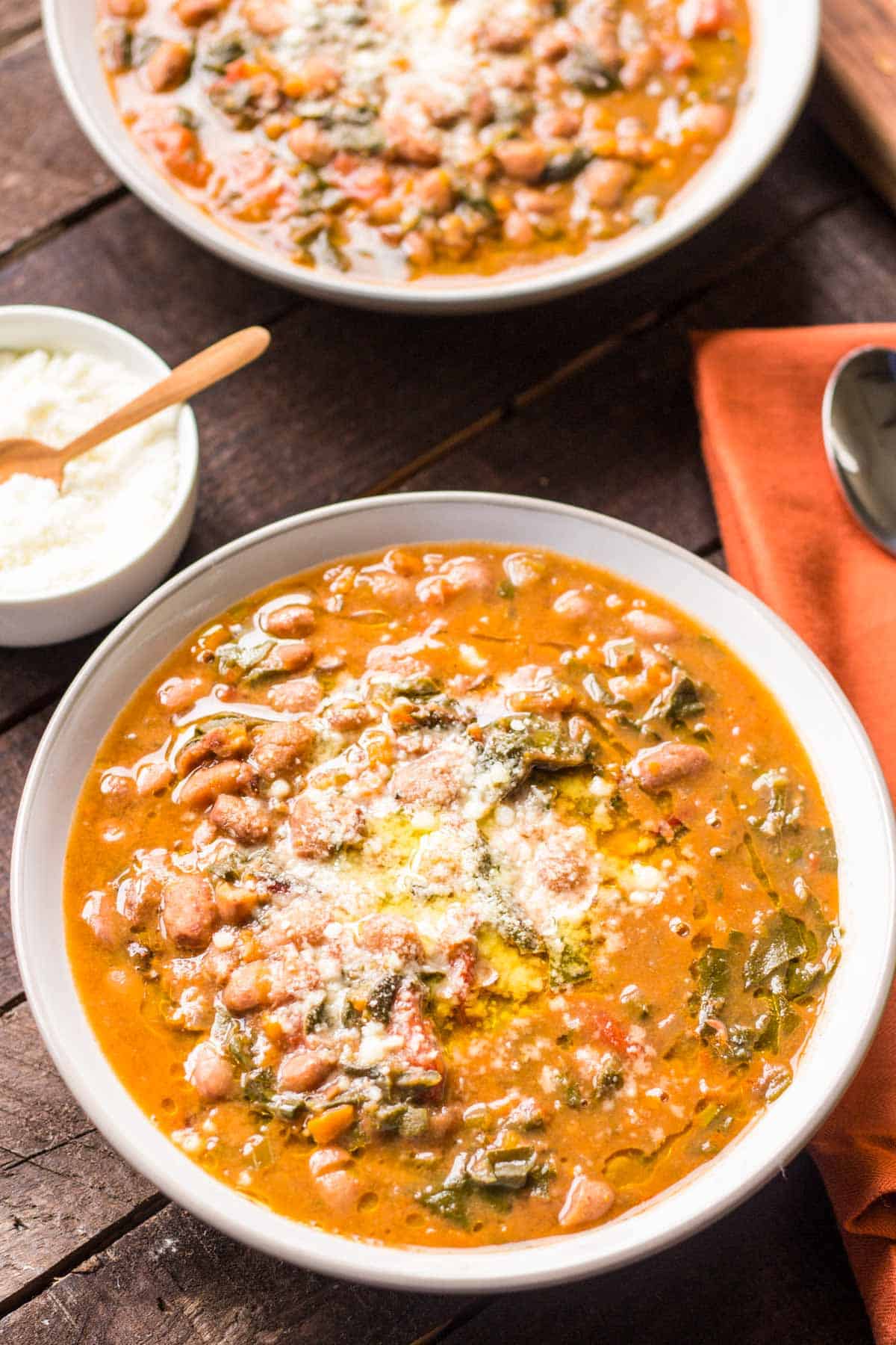 A bowl of Tuscan bean and kale soup with a bowl of grated cheese next to it.