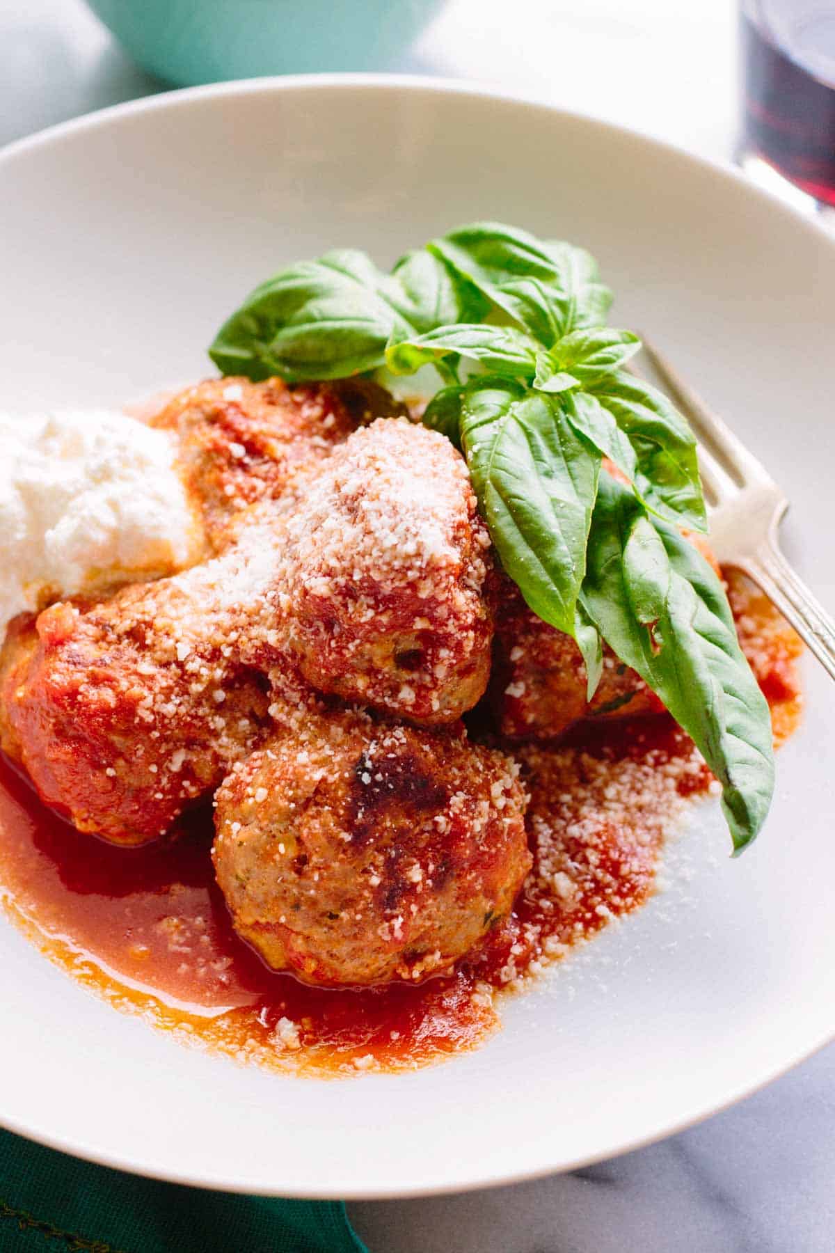 Bowl of meatballs in marinara sauce with a big sprig of basil to garnish.