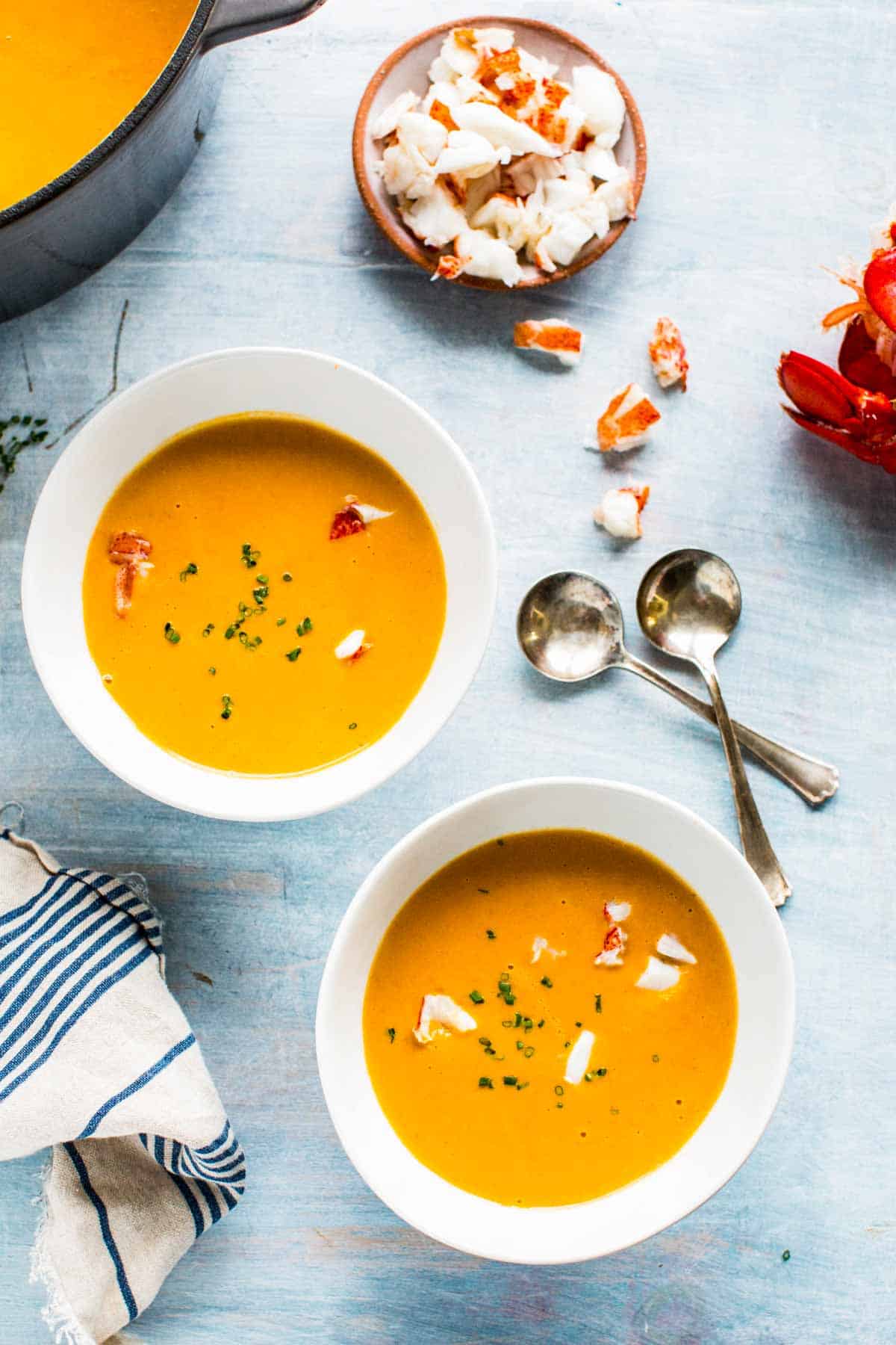 Two bowls of lobster bisque with two spoons criss crossed and a few chunks of lobster meat.