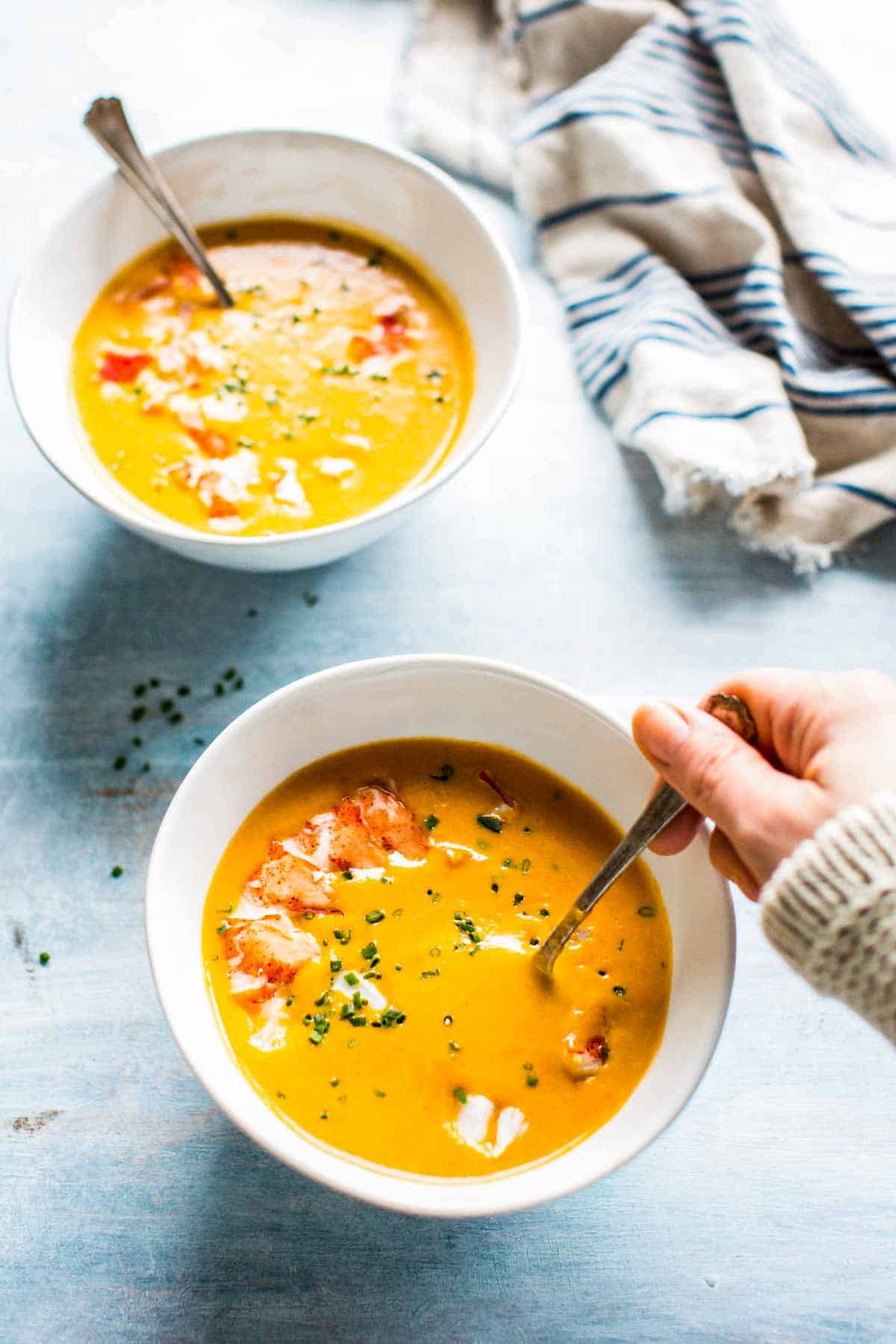 A hand holding a spoon in a bowl of lobster bisque.