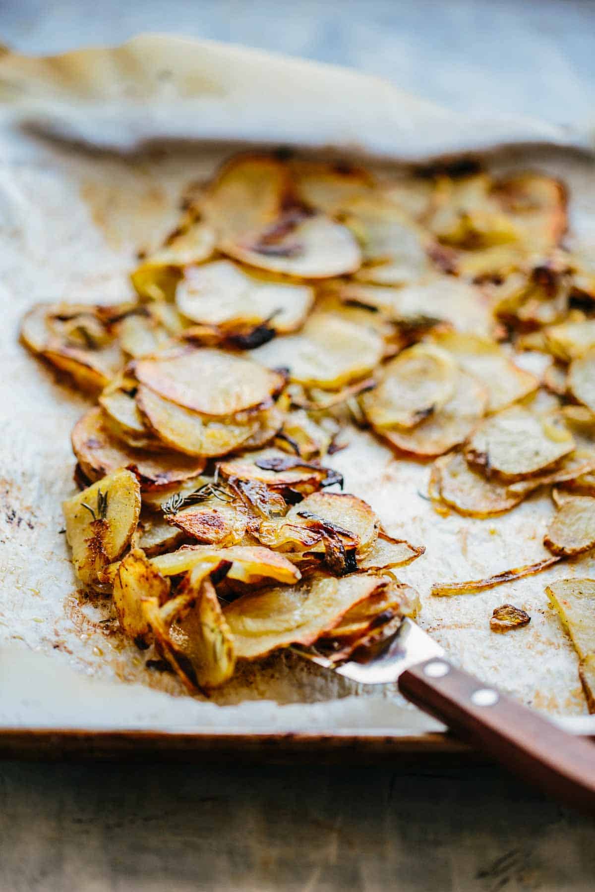 A close up of roasted potatoes and onions on a spatula.