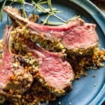 Lamb chops crusted with herbed Dijon cut off a rack and set on a blue dinner plate.
