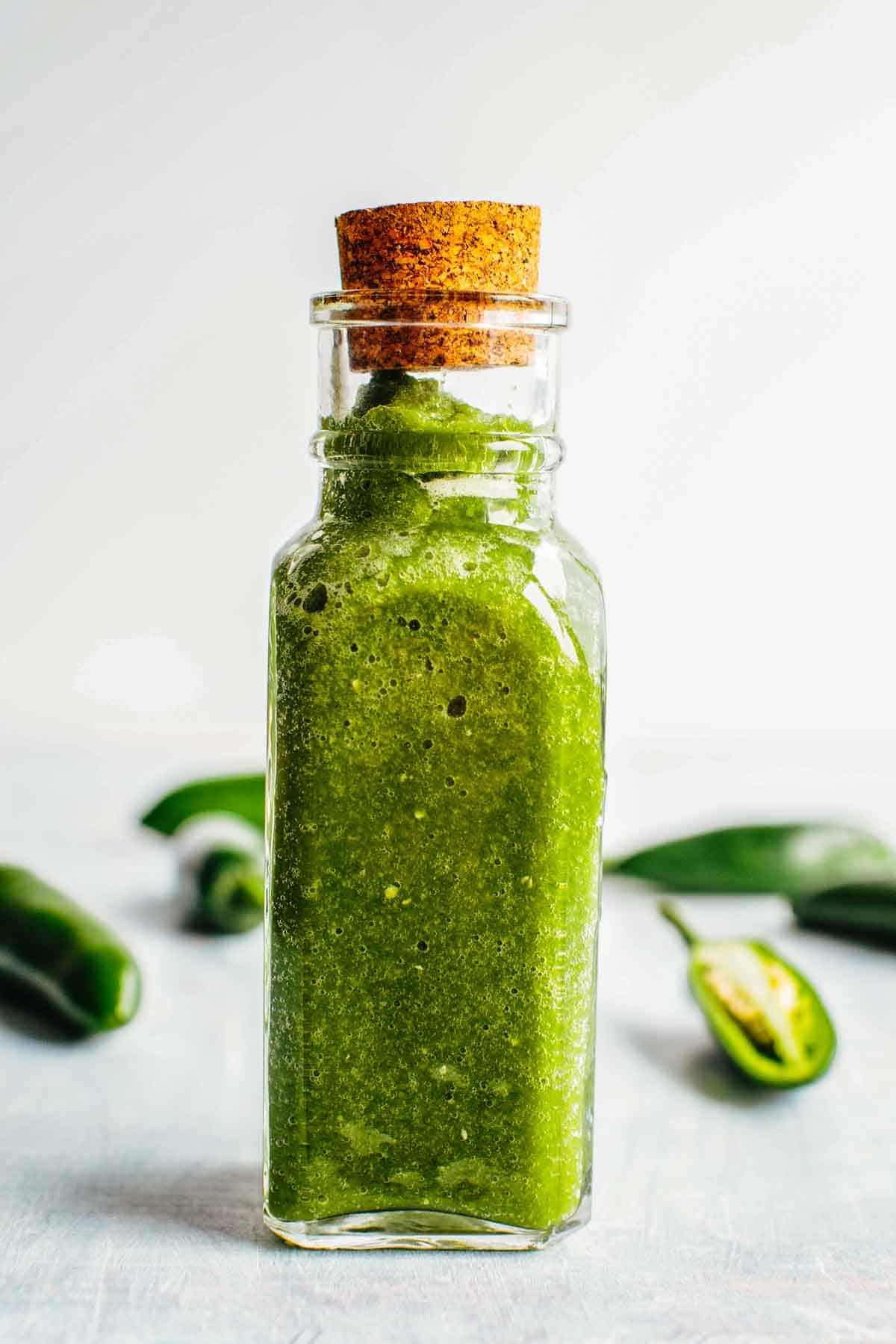 A corked bottle of Jalapeño hot sauce with fresh jalapeños in the background.