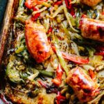 A close up of Italian sausage, peppers and onions on a sheet pan.