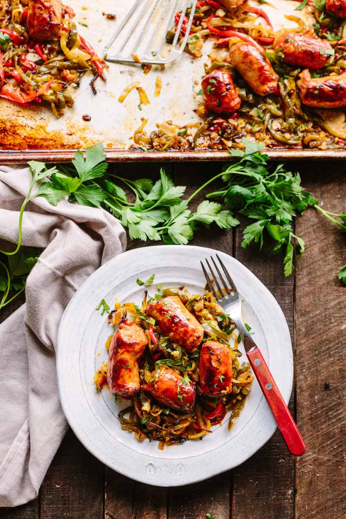 A gray plate of sausage and peppers with a fork and a sheet pan in the background.