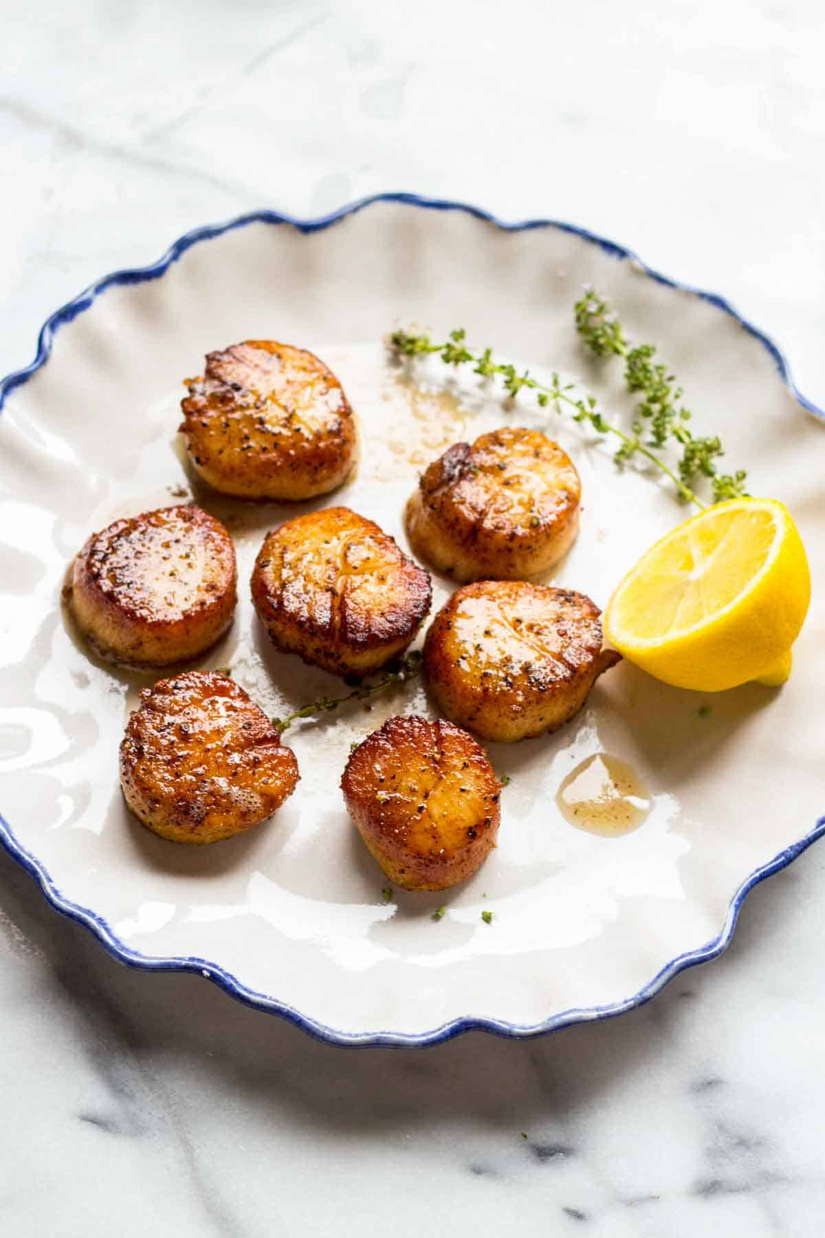Blue edged white dinner plate with pan seared scallops and a lemon half.