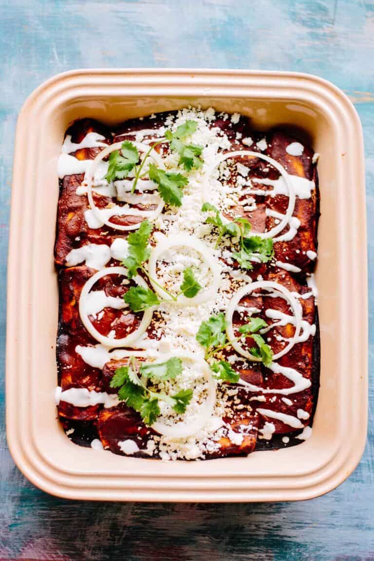 Close up of stoneware baking dish filled with baked chicken mole enchiladas topped with sour cream and cilantro.