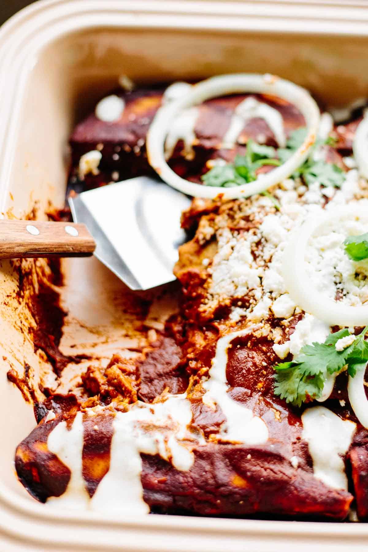Close up of a spatula in a baking dish of chicken mole enchiladas.