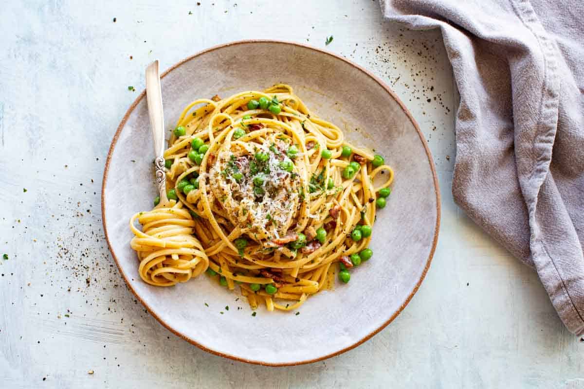 Overhead shot of a plate of pasta with peas and a fork with pasta twisted around it.