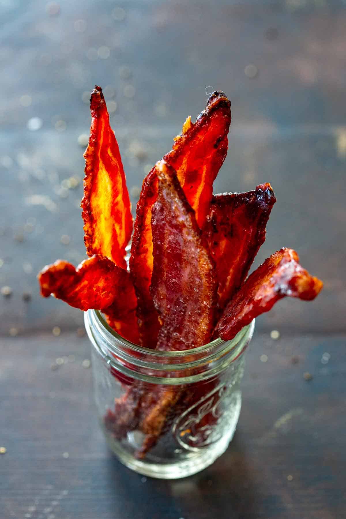 Side view of a mason jar filled with thick cut candied bacon.