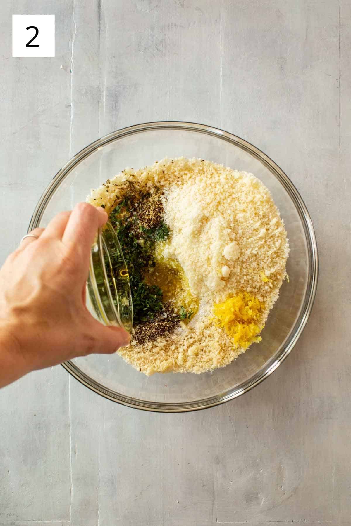 A hand drizzling olive oil into a glass bowl with other ingredients.