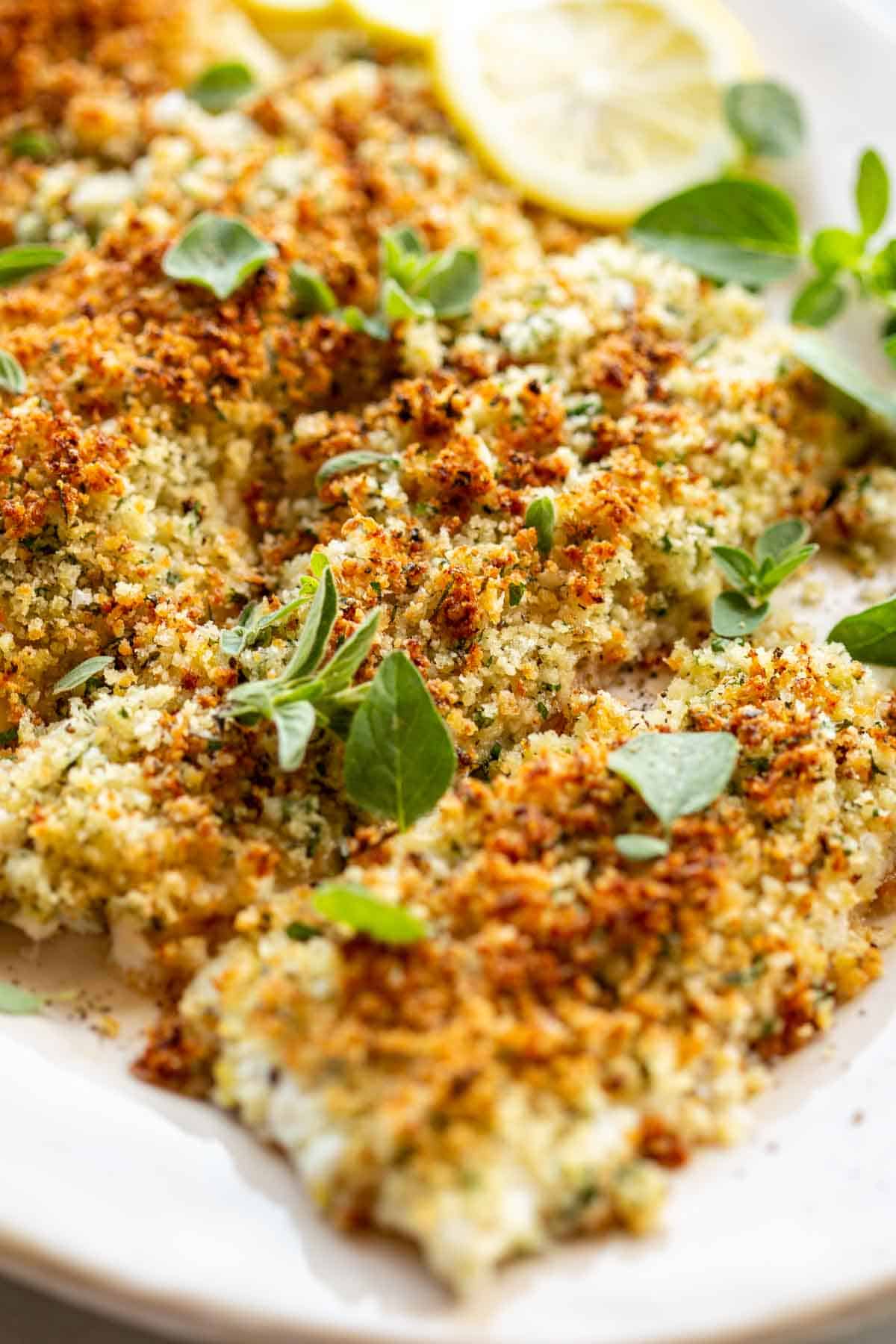 Close up of breaded flounder fillets with fresh oregano leaves.