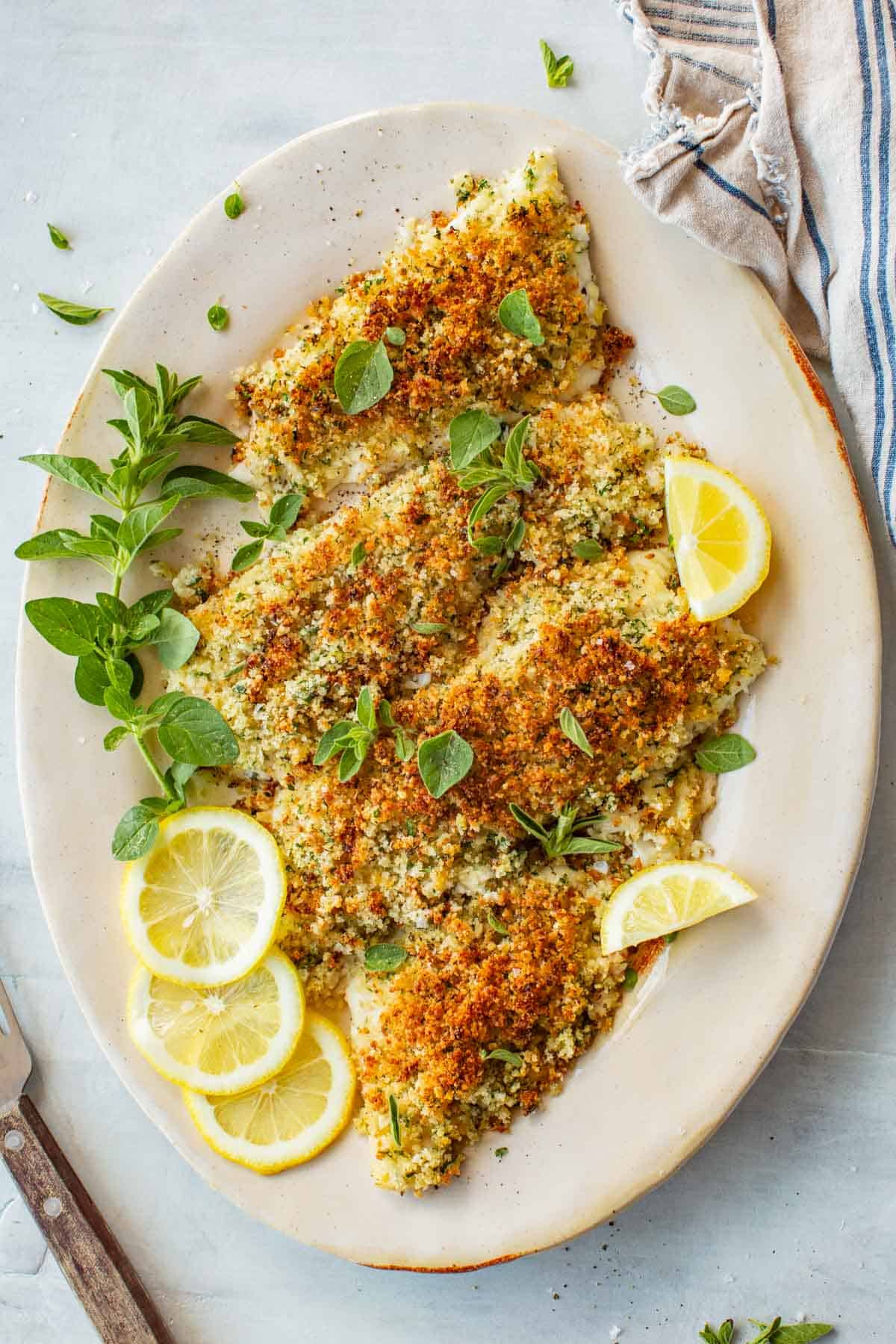 Top view of a large platter of flounder oreganata with lemon slices.