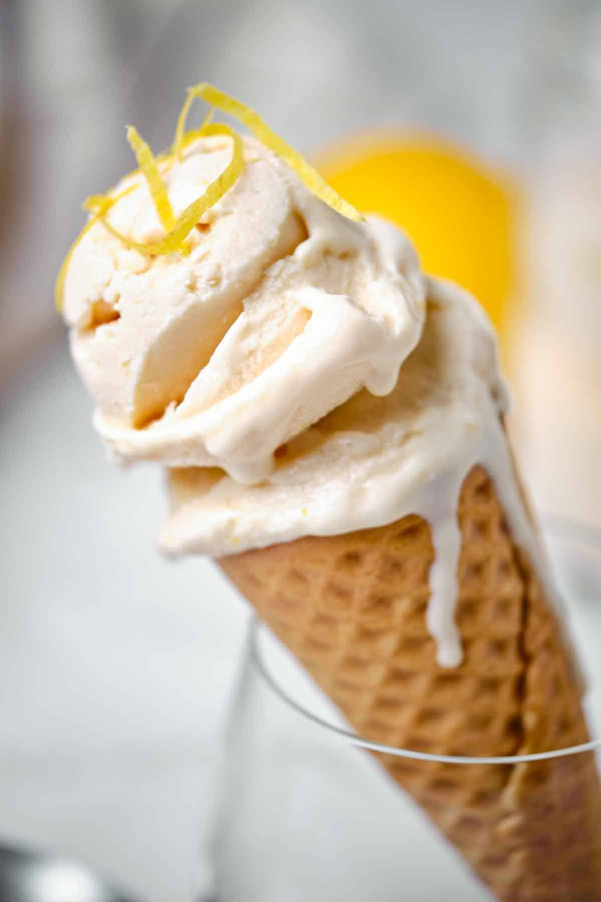 Close up of a scoop of lemon ice cream in an ice cream cone garnished with lemon zest.