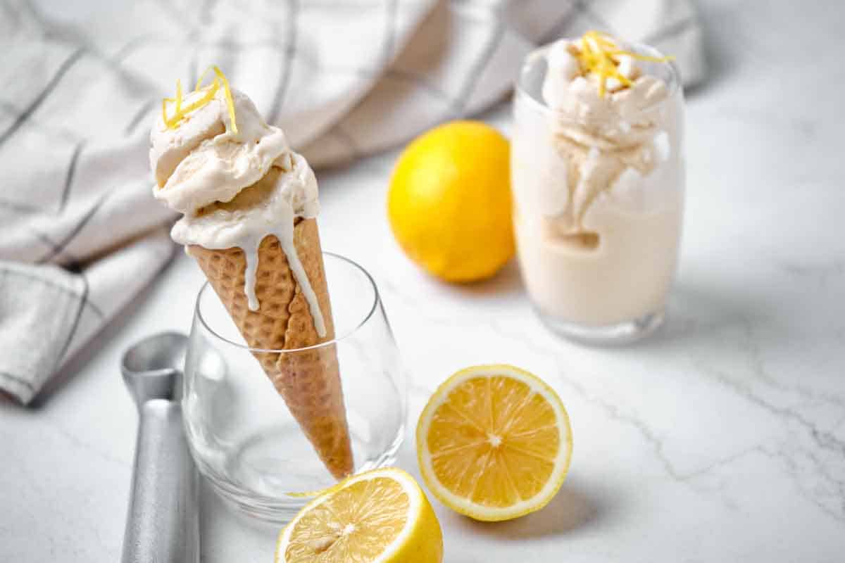 A clear glass holding an ice cream cone with another glass filled with ice cream and lemons to garnish.