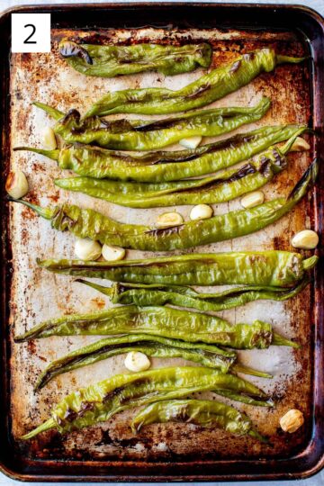 Top view of a sheet pan with roasted long hot peppers and garlic.