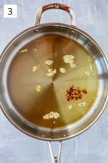 A pan with sliced garlic and chili flakes sautéing in olive oil.