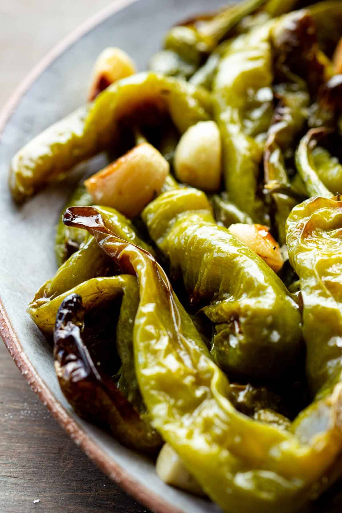 A close up of roasted Italian long hot peppers with garlic on a plate.
